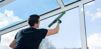 Cleaner spraying and wiping a glass window